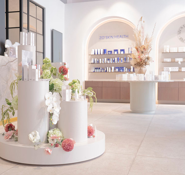 Billedet viser Cerix' lyse, moderne klinikreception med skønhedsprodukter på runde diske og hylder, dekorative blomsterarrangementer og ZO Skin Health-skilte. Stemningen er indbydende og klinisk; fokus på ansigtsbehandlinger som Botox og hudpleje i en eksklusiv, professionel ramme tilbydes af Cerix-specialister og personlig rådgivning til efterbehandling.