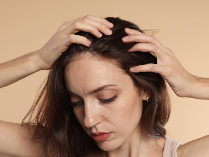 Nærbillede af en kvinde med fregner, der kører fingrene gennem sit brune hår og undersøger sin hovedbund. Hendes blik er vendt nedad. Billedet illustrerer fokus på hår hos Cerix, hvor der tilbydes professionel vejledning og effektive behandlinger mod hårtab og forbedring af hårets sundhed.