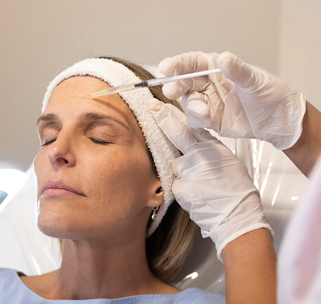 Billede af en kvinde liggende med lukkede øjne mens en behandler fra Cerix i hvide handsker giver en Botox-injektion i panden. Fokus på ansigtets fine linjer, sterile miljø og præcis nåleteknik under kosmetisk behandling tilpasset moden hud i klinisk opsyn.