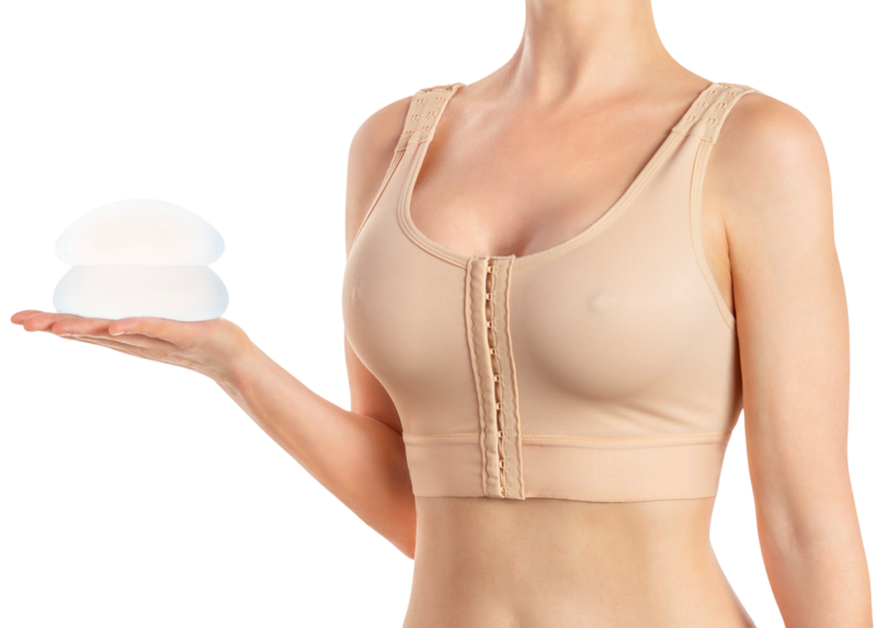 Dette billede fra Cerix viser en kvinde iført en beige post-operativ kompressions-bh, der holder to silikone brystimplantater i sin åbne hånd. Motivet illustrerer processen omkring en brystforstørrende operation (BFO), hvor implantater benyttes til at forstørre brysterne.