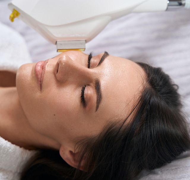 På Cerix-klinikken ligger en kvinde afslappet med lukkede øjne, mens et håndholdt laser-/IPL-apparat føres over hendes ansigt. Billedet viser en ansigtsbehandling koncentreret om pande, næse og kinder. Proceduren er ikke-invasiv, til hudfornyelse, pigmentudjævning og mild opstramning, med fokus på sikkerhed og komfort.