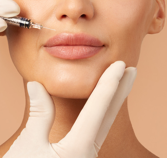 Cerix: Nærbillede af ansigt med fokus på læber og hage, hvor handske‑klædte hænder holder hagen, mens en sprøjte forberedes til læbeforstørrelse med filler. Billedet illustrerer kosmetisk behandling af ansigtet og sterile procedurer hos Cerix. Viser præcis injektionsplacering og professionelle teknikker.