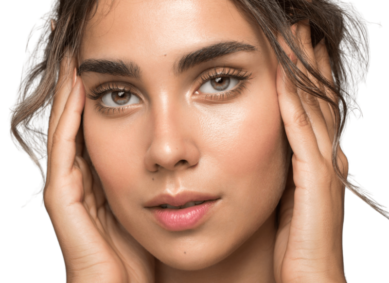 Et nærbillede af en ung kvindes ansigt med klar, strålende hud og naturlige øjenbryn, hvor hænderne blidt indrammer ansigtet. Dette billede illustrerer de naturlige skønhedsresultater, der kan opnås gennem professionelle ansigtsbehandlinger hos Cerix, såsom hudforyngelse, fillers eller Botox for et friskt og velplejet look.