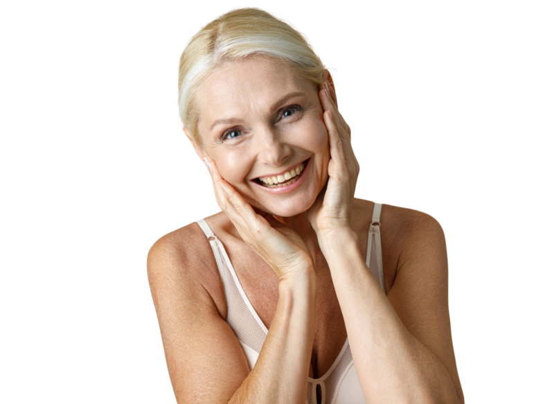Portræt af en glad, moden kvinde, der rører ved sine kinder og kæbelinje med begge hænder. Billedet illustrerer effekten af anti-age behandlinger til ansigtet hos Cerix, såsom hudforyngelse eller fillers, der giver et opstrammet og friskt udseende. Hun bærer en lys top mod en hvid baggrund.