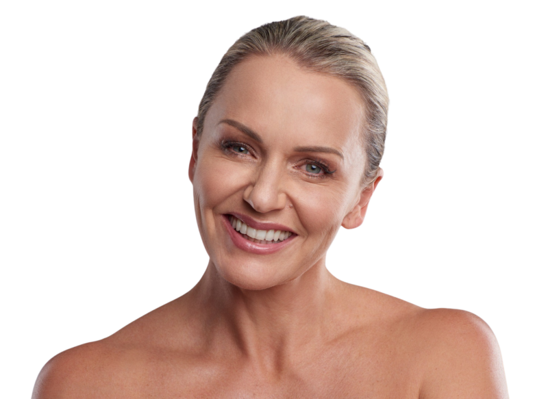 Et nærbillede af en smilende, moden kvinde med lyst hår, der kigger direkte i kameraet med bare skuldre. Billedet viser en velplejet hud i ansigtet, hvilket kan være et eksempel på resultater fra kosmetiske behandlinger som Botox, fillers eller hudforyngelse til ansigt og hud hos Cerix.