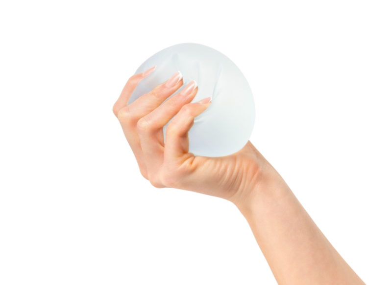 Et nærbillede af en hånd, der holder og klemmer et klart, rundt silikone brystimplantat mod en sort baggrund. Billedet illustrerer de højkvalitetsimplantater, der anvendes af specialisterne hos Cerix i forbindelse med en brystforstørrende operation (BFO) for at opnå det ønskede resultat for brystet.