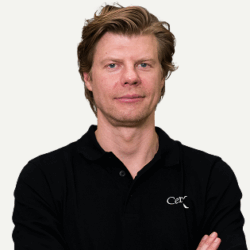 Dette billede viser en mandlig specialist fra Cerix. Han bærer en sort polo med Cerix-logoet på brystet og står med armene over kors mens han kigger direkte i kameraet. Hans ansigt og hår er i fokus, og han repræsenterer klinikkens ekspertise inden for kosmetiske behandlinger til ansigt og krop.